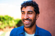© Nexa - Portrait of a happy young man with curly hair and a beard smiling outdoors in warm light.