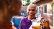 © Nexa - Happy senior African American man clinking beer glasses with a friend at an outdoor backyard party.