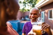 © Nexa - Happy senior African American man smiling and toasting with a glass of beer during a backyard party on a sunny day.