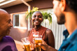 © Nexa - Smiling African American woman with shaved head enjoying a beer with family and friends at an outdoor backyard gathering during golden hour.