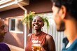 © Nexa - Happy Black woman with a shaved head smiling and holding a beer at an outdoor backyard party with friends.