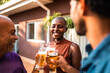 © Nexa - Happy multi-generational Black family or friends toasting with beer glasses during a backyard barbecue party at sunset.