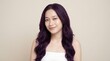© satrio - A young woman with long wavy dark purple hair smiles gently, wearing a white strapless top against a plain background.