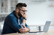 © Prostock-studio - Attractive tired bored programmer digital specialist manager work remotely online overtime. Concentrated sad pensive young bearded guy looks at laptop and presses hand to mouth in kitchen interior