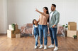 © Prostock-studio - Young Homeowners Concept. Excited young family of three people planning interior, decorations and furniture in their own house, standing in empty living room, woman pointing up at free copy space