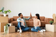 © Prostock-studio - Good Job Concept. Happy young couple tenants giving high five, celebrating moving day, sitting on the floor near carboard boxes and plants. Smiling man and woman enjoying relocation