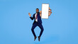 © Prostock-studio - A young man dressed in a suit jumps with excitement while holding a blank smartphone. He has a big smile on his face, and the vibrant blue background enhances the cheerful mood of the moment.