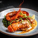 Close-up of grilled crustaceans on a plate, garnished with greens, sauce, and a lemon wedge, against a dark backdrop