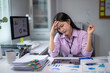 © Wasana - Young professional woman suffering from headache while working with financial data in modern office