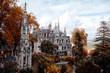 © Loginova - Quinta da Regaleira palace and chapel rising above autumn trees and gardens under partly cloudy sky in Sintra, Portugal.