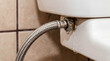 © Aurora Aesthetics - Leaking flexible water hose on toilet plumbing emergency repair maintenance house damage accident flood insurance claim professional plumber service background