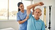 © creative - An older man in blue shirt raises arm during therapy, assisted by a nurse at clinic. A female physical therapist helps an elderly man stretch his arm. Clinic setting.