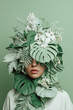 © Irina - Unique fashion statement with model wearing vibrant green foliage headdress adorned with white flowers and leaf textures. Artistic embodiment of nature with creative leafy design,