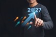 © Meow Creations - Man touching virtual 2027 year target with upward arrows representing business growth and future goals