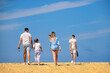 © Elena - A family of four in white and blue outfits walks across a hot dry rocky desert against a blue sky, father holding daughter's hand.