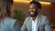 © Maryna - Black man in suit laughs with person at desk. They are in a modern office, discussing business or service. Interaction looks positive and friendly.