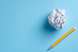 © 윤미 김 - Top view flat lay of crumpled white paper ball and yellow pencil on blue background representing writer's block and creativity