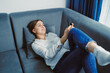 © DSMT - Woman relaxes on couch while using smartphone in living room during daytime