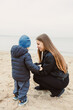 © DSMT - Woman talks with young boy on sandy beach near water during cloudy day in cool weather