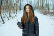 © DSMT - Woman stands in snowy forest holding a drink while smiling on a winter day with trees in the background