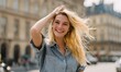 © simba kim - A beautiful young blonde woman walking joyfully through stylish Parisian streets, running her fingers through her hair
