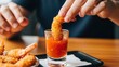 © AFFANYUDA - Close-up of hand dipping crispy fried shrimp into red chili sauce