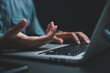 © sorapop - Close-up of hand gesturing over laptop keyboard, dark background.
