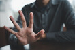 © sorapop - Closeup of a man's hand with fingers spread out in a stop gesture. The man is wearing a grey shirt and the background is blurred. .
