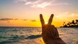 © zainal - Hand showing peace sign against vibrant sunset over ocean waves.