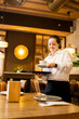 ©  Yistocking - A young woman between 20 and 30 years old with Down syndrome is working as a waitress in a restaurant.Vertical photo of a girl about to pick up a coffee cup from a tray. Concept of trisomy 21.