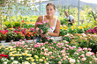 © JackF - Girl in sales area of flower exhibition examines rose flower, chooses plants for landscaping apartment, front garden. Exhibition and sale, self-service store with plants and related products