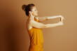 © Alliance - A middle-aged woman in mustard yellow activewear performs a focused wrist and forearm stretch. Her interlocked hands and closed eyes convey calm mindfulness and well-being.