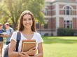 © Alingga - Smiling female student stands on campus holding college textbooks happily