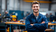 © Selvi - Smiling young man with light brown hair and a beard, wearing a blue work jacket, standing confidently in a workshop environment with tools and equipment in the background