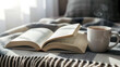 © inktrek - Cozy reading setup with open book and steaming mug on plaid blanket