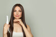 © artmim - Gorgeous woman brunette with long straight smooth hairstyle using hair straightener iron on light grey background