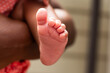 © Jeanne Sager Photo - Detail of a newborn's small foot, showcasing delicate skin and perfectly formed miniature toes. The arm of the baby's mother tenderly cradling her child is in soft focus in the background.