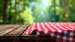 © florynstudio3 - Wooden table draped with a red-and-white checkered cloth, blurry green forest in background