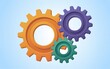 © Fahad - Interconnected gears in orange, purple, and green, symbolizing collaborative machinery, against a soft blue background from a straightforward viewpoint