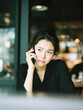 © Kowit - A woman with a serious expression is engaged in a phone conversation, showcasing her emotions in a modern cafe setting.