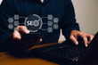 © Minttita - A person using a smartphone and laptop, with SEO-related graphics displayed, emphasizing digital marketing and online presence.