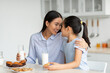 © Prostock-studio - Happy loving asian mother and little daughter eating snacks in kitchen together, young mom and her cute female child enjoying tasty cookies with milk