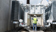 © JD Studio - Professional engineer inspecting control panel and monitoring gauges of power transformer at high voltage substation to ensure industrial energy infrastructure and grid safety.