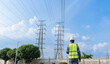 © JD Studio - Back view of electrical engineer looking at high voltage power line pylon under blue sky. Maintenance worker planning grid infrastructure development and energy distribution.