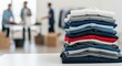 © Mey - A stack of folded clothes on a table in a room with three men in the background.