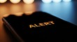 © abu - Close up of a black smartphone displaying an orange alert message, set against a blurred bokeh background with soft lighting, indicating a digital notification or warning.