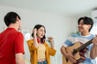 © Kawee - Diverse Asian friends playing guitar and dancing in living room at home.