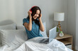 © Kawee - Asian young woman listen to music and using laptop in bedroom at home.