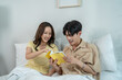 © Kawee - Asian beautiful couple sitting on bed and reading book together in house.