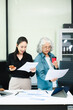 © Nuttapong punna - Asian businesswomen reviewing documents in modern office. Mentoring, consulting and teamwork concept with laptop and tablet. Corporate collaboration